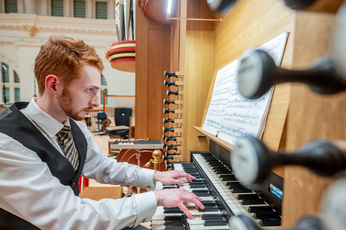 A male student, playing the organ in the RCM, wearing smart attire.